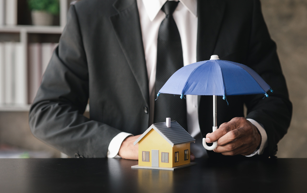 Businessman holding umbrella over model house symbolizing property manager as additional insured for landlord protection